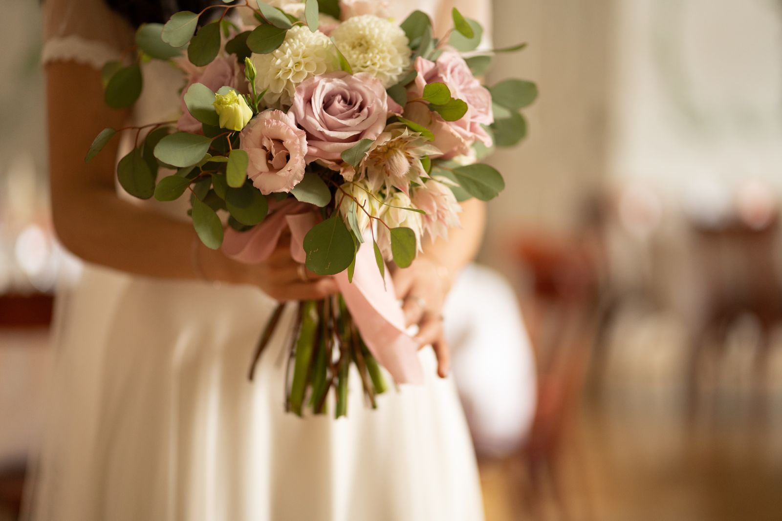 A bride in an ivory dress holding a bouquet of dusty-pink roses, lisianthus and eucalyptus