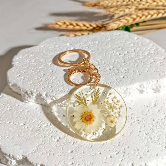 A round clear resin keychain holding a small white daisy and baby's breath